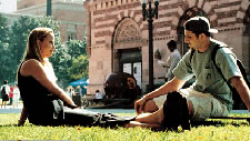 Two students converse on a grassy campus area.