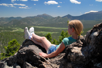 A girl relaxes on a rocky outcrop, enjoying a mountain vista.
