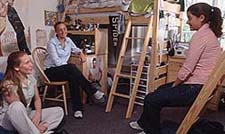 Three young women are sitting and talking in a dorm room.